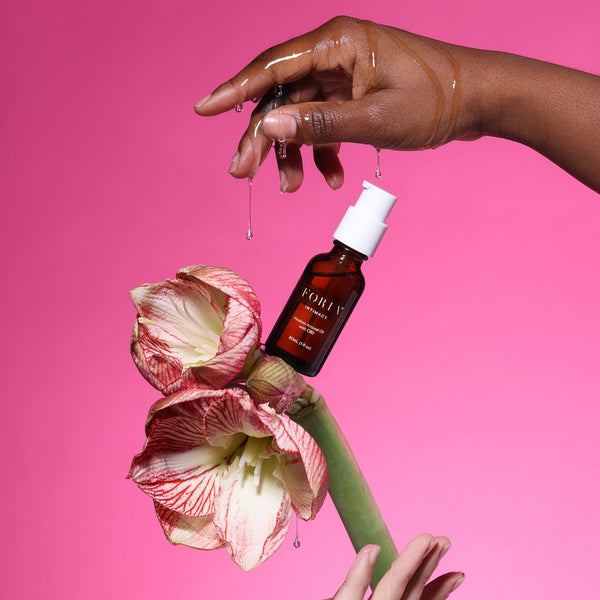 Foria Awaken Arousal Oil Hand holding a flower dripping for best sex on a pink background