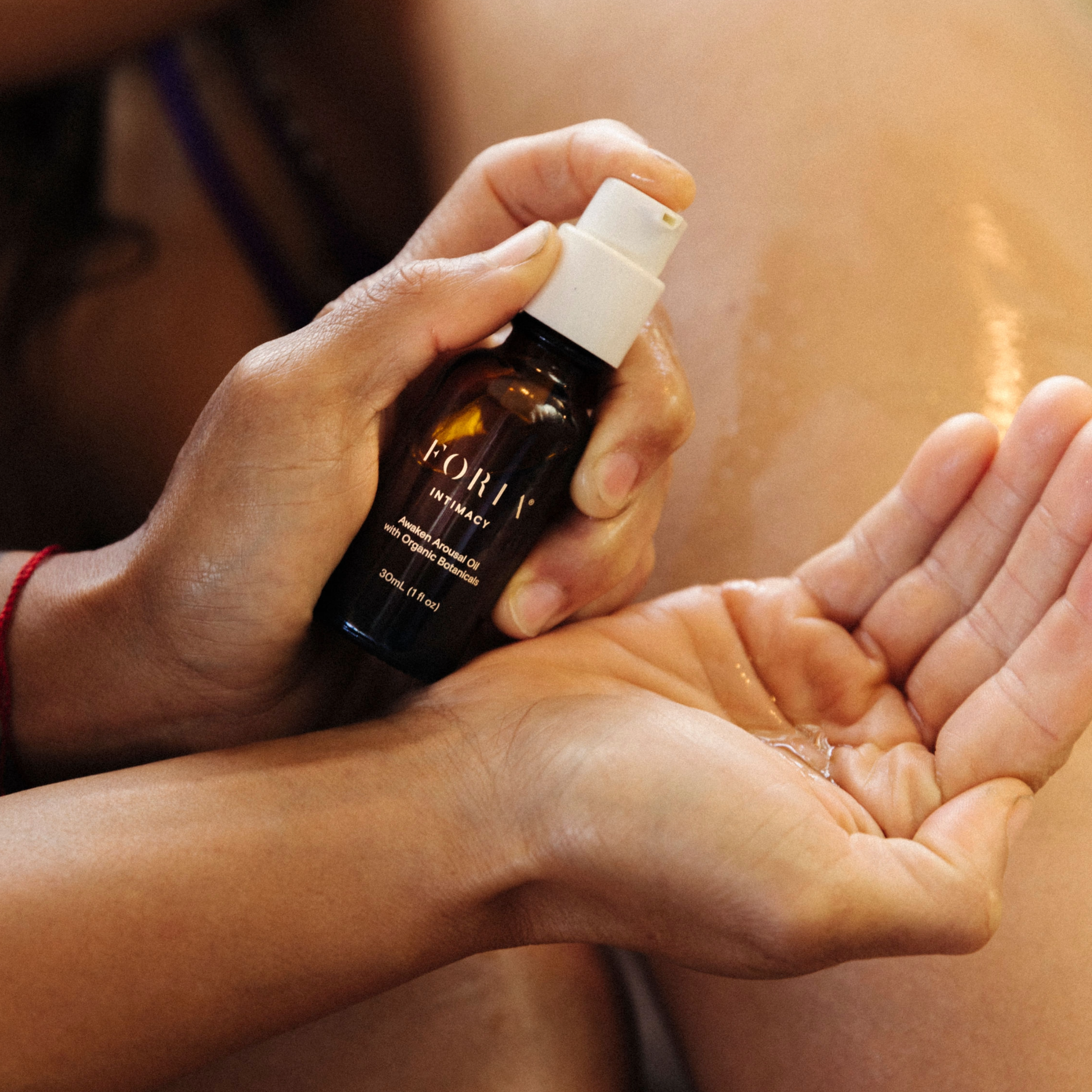 Foria Pleasure Set Awaken Arousal Oil with hand holding bottle and other hand holding oil. 