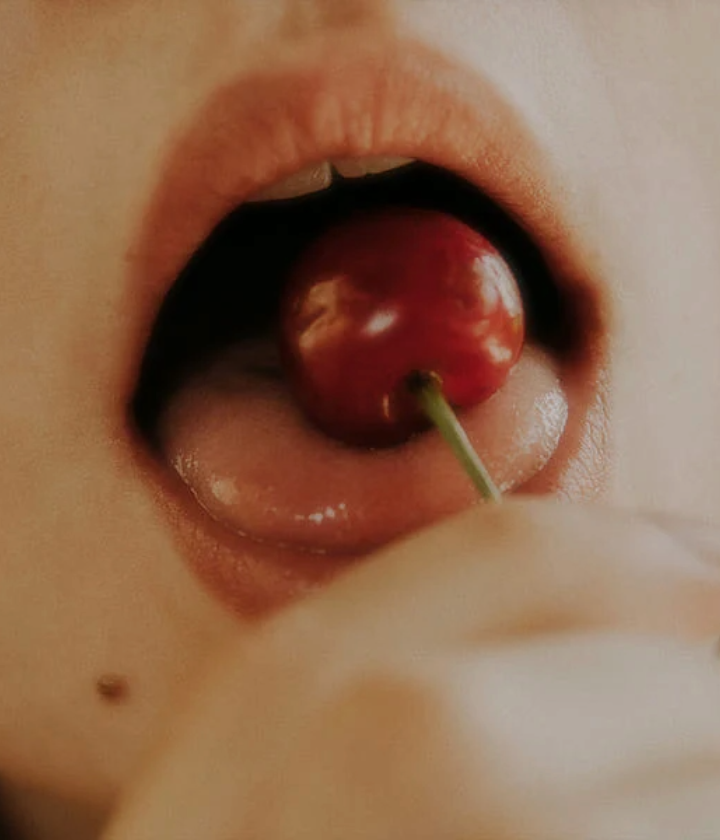 Close-up of a person's mouth with a cherry inside. Foria blog on orgasms.