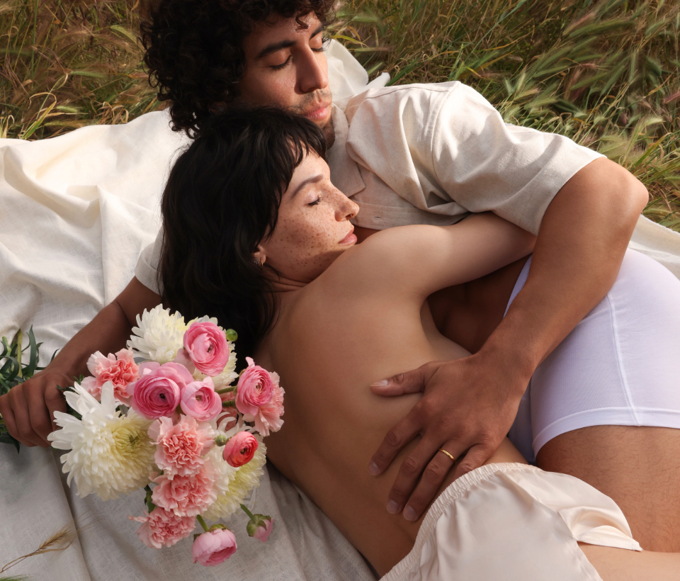 Foria is for deeper connection and enhanced pleasure. Couple lying in a field with a woman holding flowers