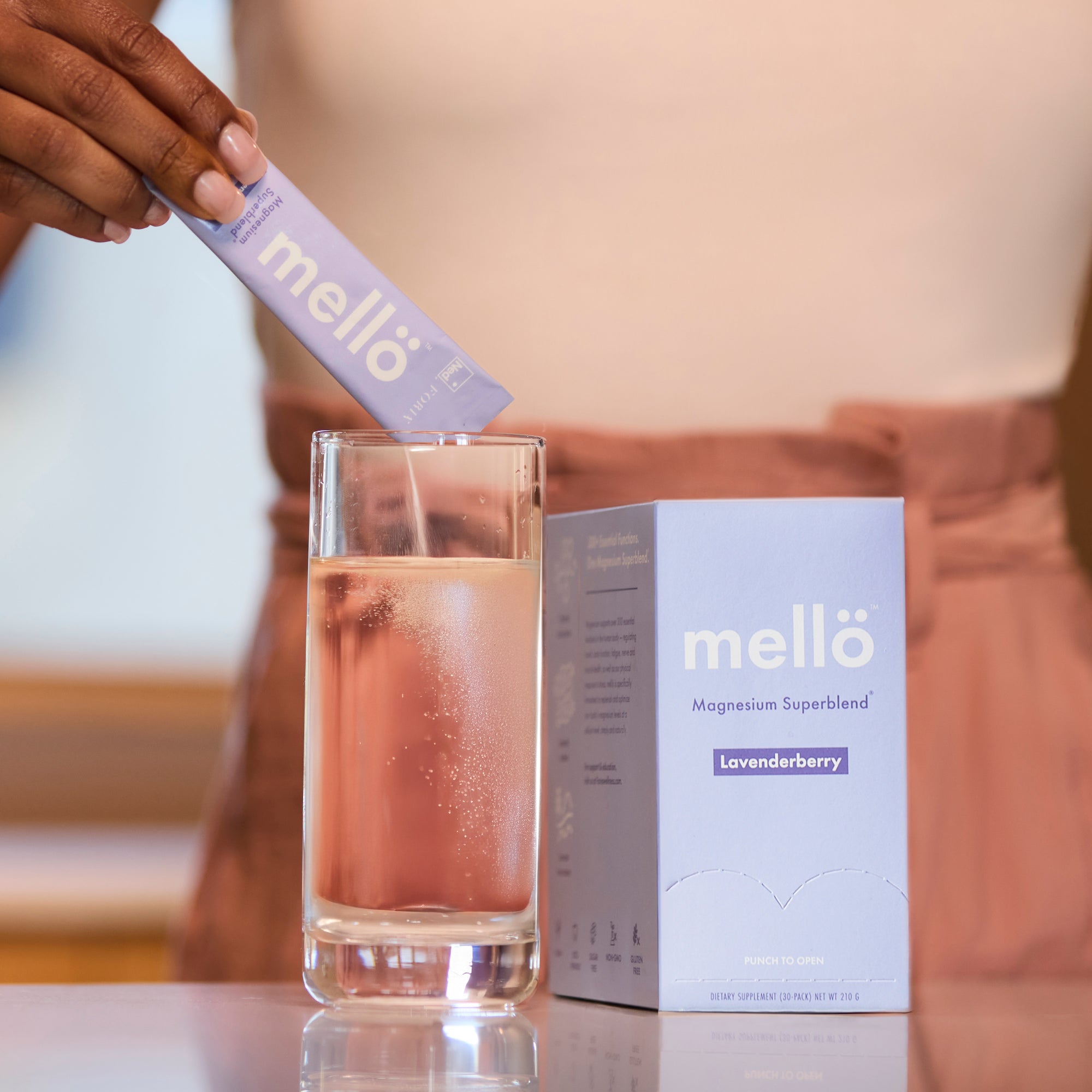 Person pouring a mello magnesium into a glass of water with the mello box in the background.