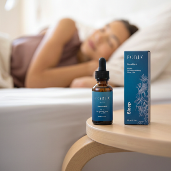 Foria Sleep Blend Deeper Sleep with CBD bottle and box on a table with a blurred background of a person lying down.