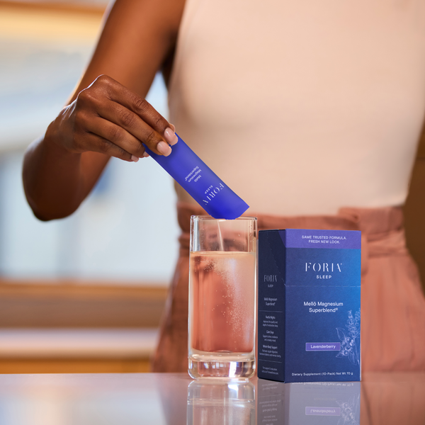 Foria Mellö Magnesium - 10 Travel Sticks Person holding a Magnesium stick with a glass of water and the product packaging.
